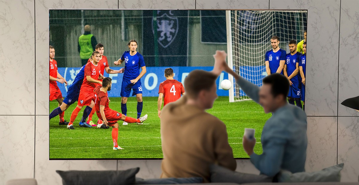 Ljudi koji gledaju sportsku utakmicu na televizoru u dnevnoj sobi na iznimno velikom televizoru